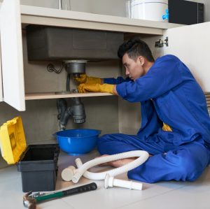 Young Vietnamese plumber checking drain in kitchen